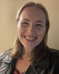 Ellie is a blonde woman with mid-length hair which she is wearing down. She has brown eyes and a wide smile.