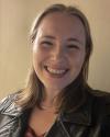 Ellie is a blonde woman with mid-length hair which she is wearing down. She has brown eyes and a wide smile.